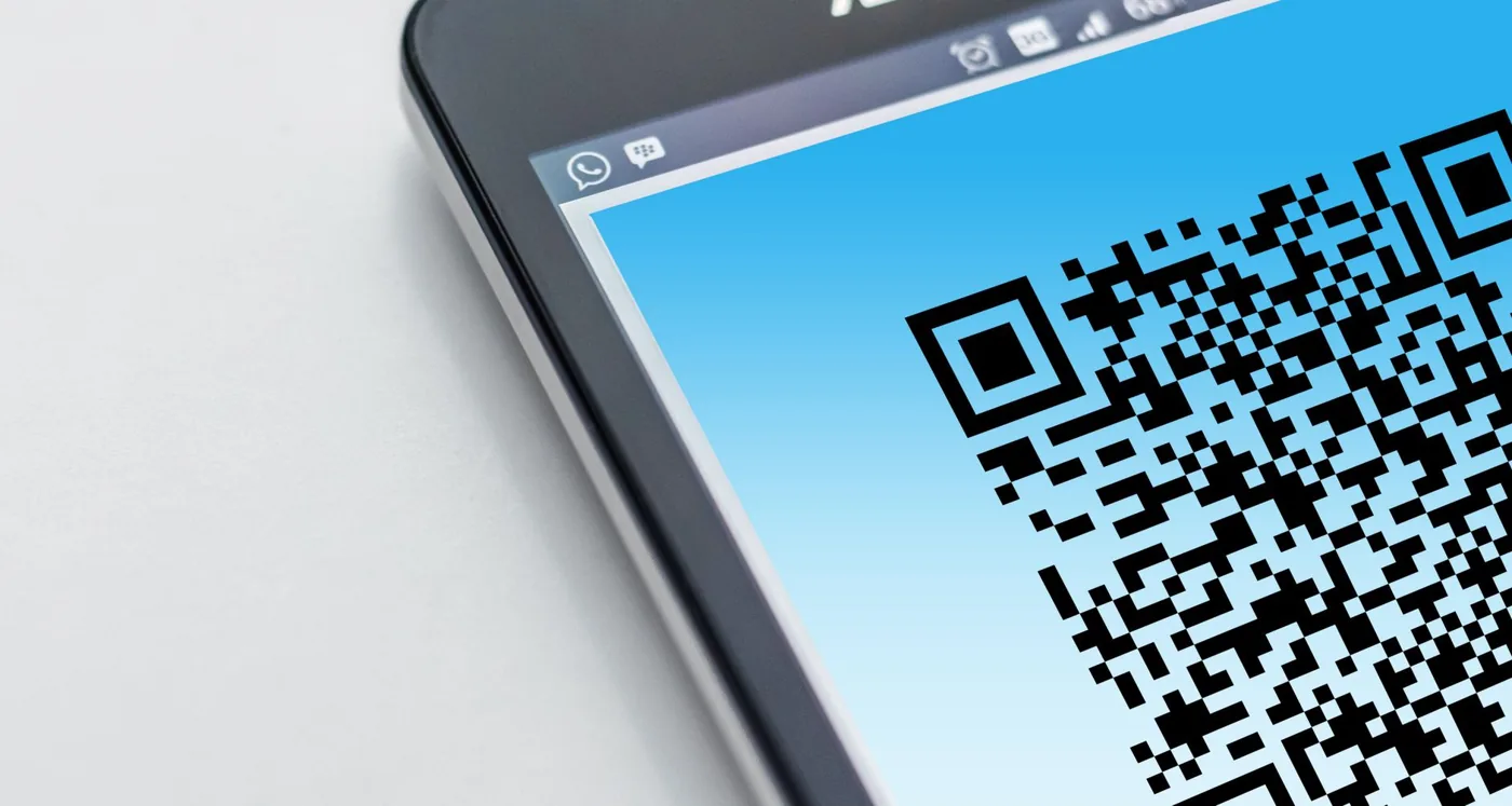 A smartphone scanning a QR code on a printed card, with a analytics dashboard visible in the background